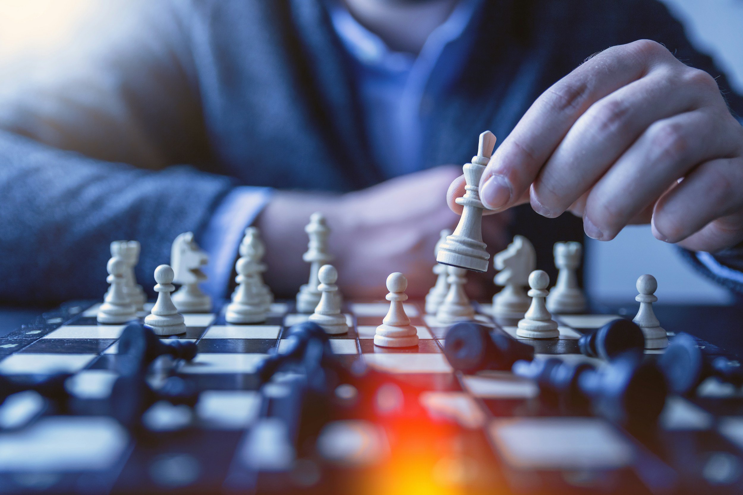 A person in a suit playing chess with a wooden chess set on a black and white board.